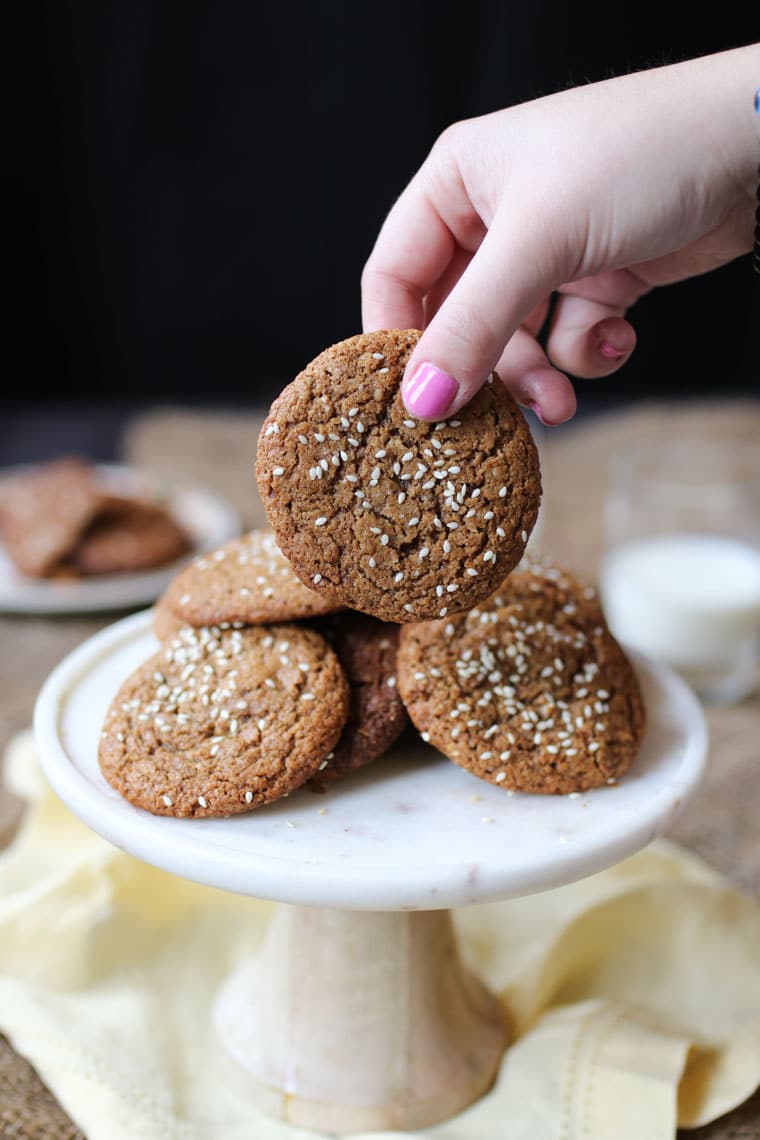 A hand picking up a vegan tahini cookie from a pile of cookies. 