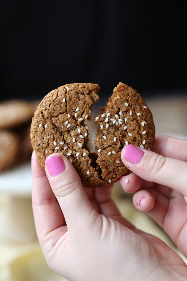 A hand breaking apart a vegan tahini cookie. 