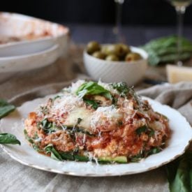 A photo of a slice of zucchini lasagna with turkey sausage ragu with grated cheese on top and basil sprinkled on.