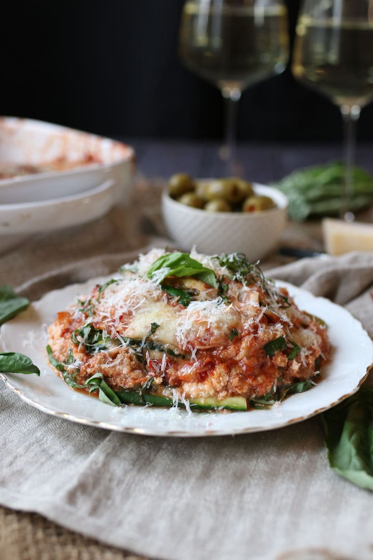 A photo of a slice of zucchini lasagna with turkey sausage ragu with grated cheese on top and basil sprinkled on.