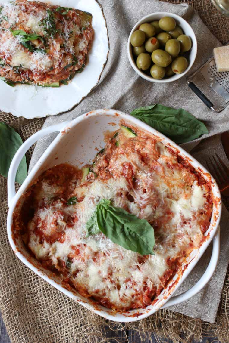 An overhead image of zucchini lasagna in a white baking dish with a piece taken out.