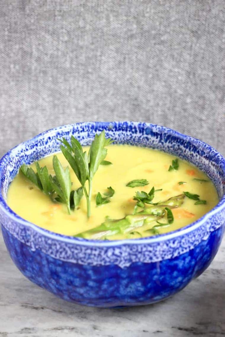 gluten free and vegan cream of asparagus soup in a blue floral bowl garnished with fresh herbs