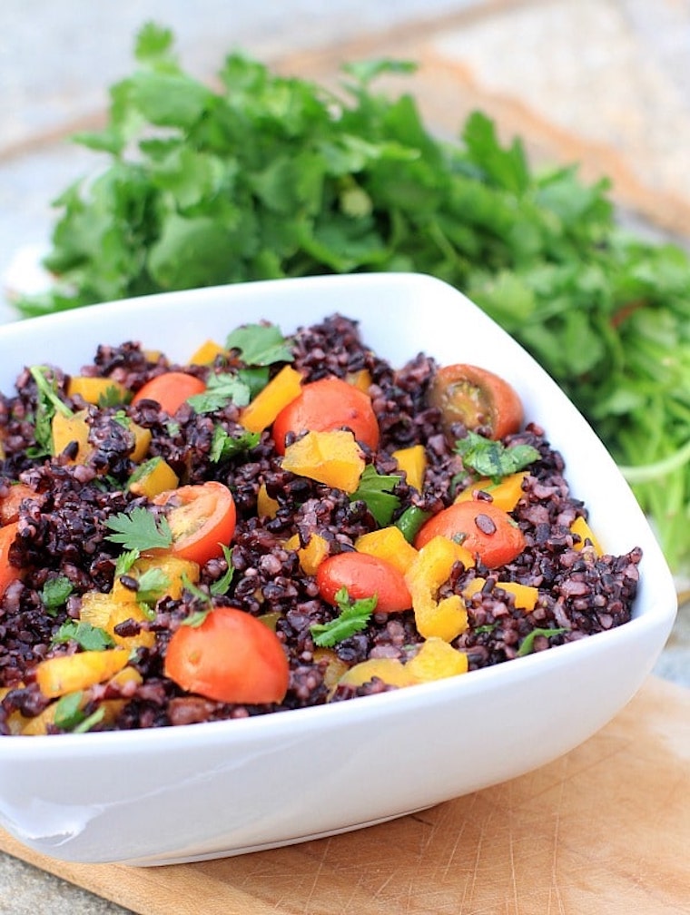 vegan low fodmap cherry tomato and forbidden rice salad served in a white bowl with fresh greens in the background