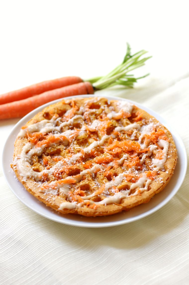 close up of vegan and gluten free carrot cake waffles for easter brunch garnished with protein frosting served on a white plate with fresh carrots on the side