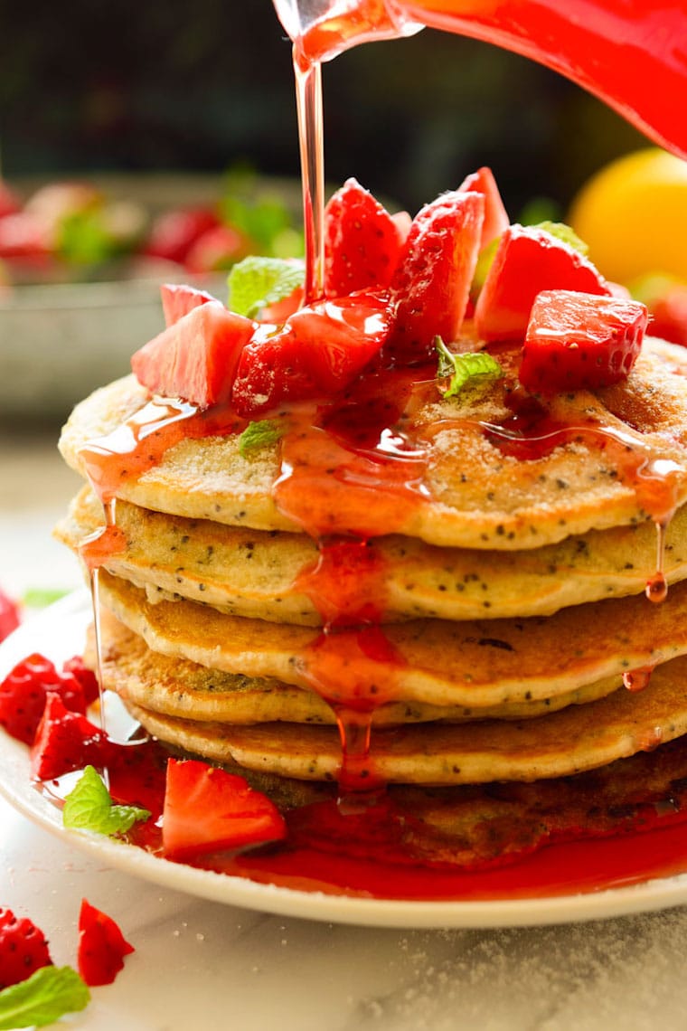 close up of a stack of strawberry lemon poppyseed pancakes for easter brunch garnished with strawberry sauce and chopped fresh strawberries