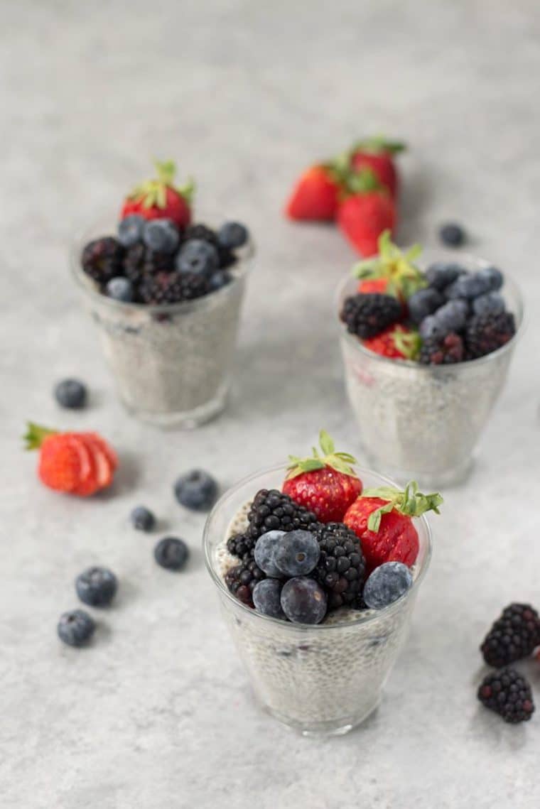 three berry flavoured soy chia puddings served in clear glasses garnished with fresh berries and herbs
