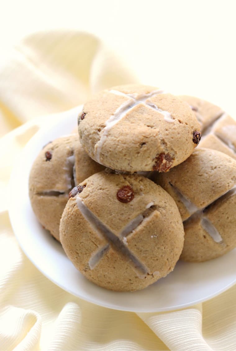 gluten free and vegan hot cross buns for easter stacked on top of one another on a white plate