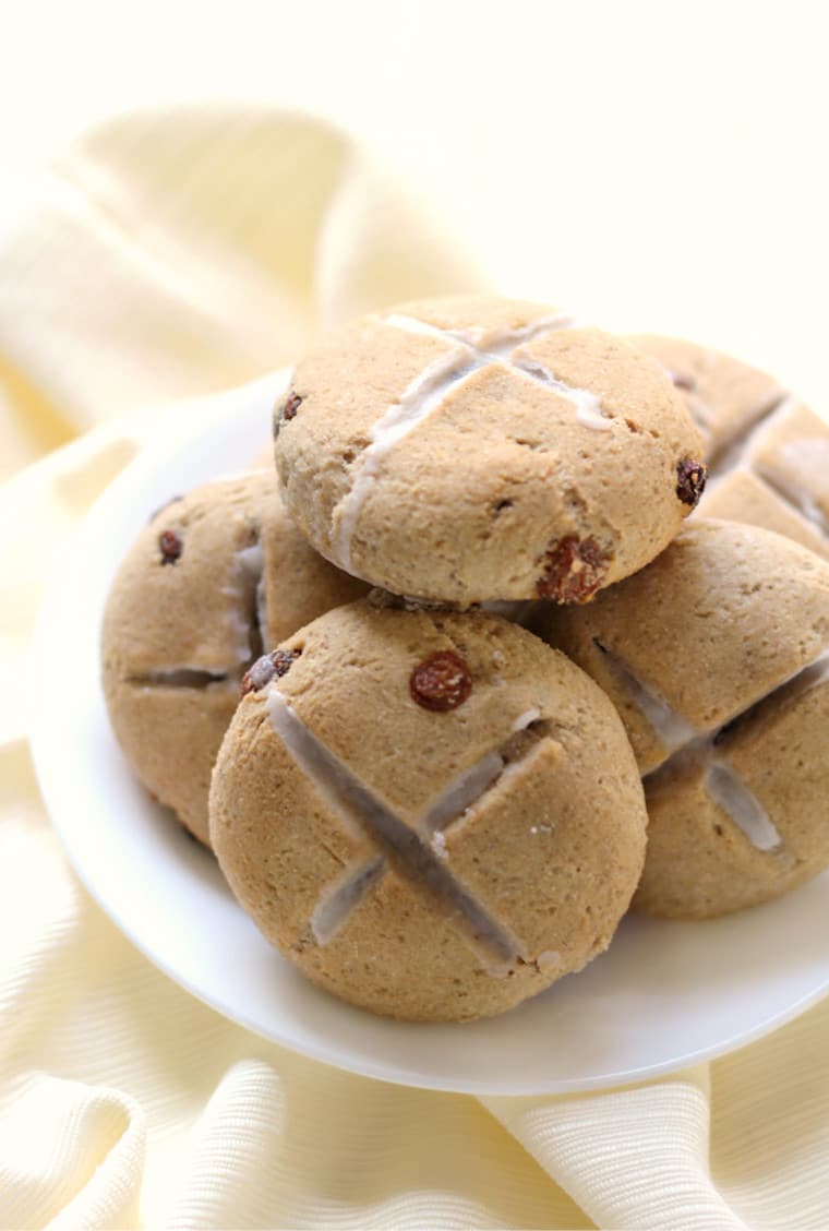 gluten free and vegan hot cross buns for easter stacked on top of one another on a white plate