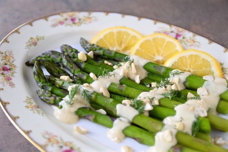 gluten free asparagus garnished with cauliflower cashew cream and lemon wedges served on a white floral plate