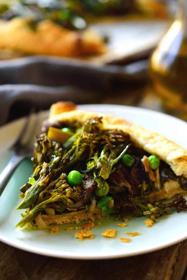 close up of a slice of spring vegan vegetable galette on a blue plate with a silver fork