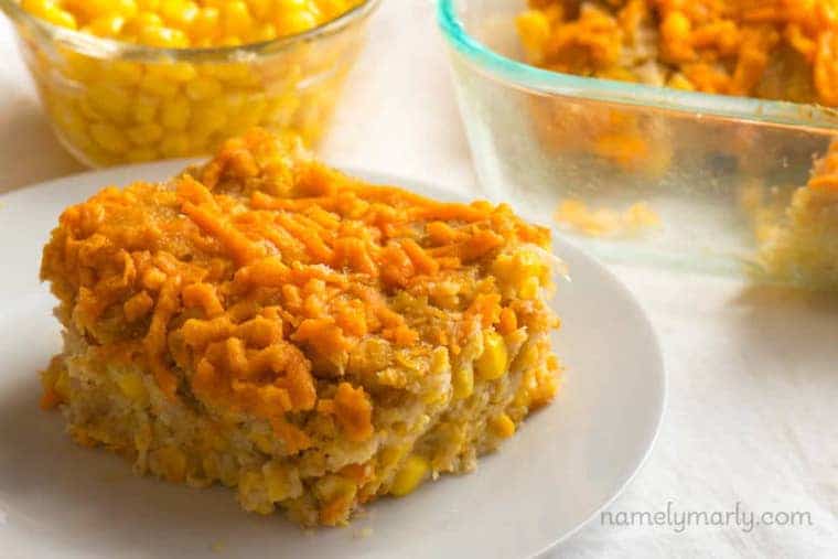 close up of slice of easy vegan corn casserole on a white dish with additional casserole in a clear dish and a clear bowl of corn in the background