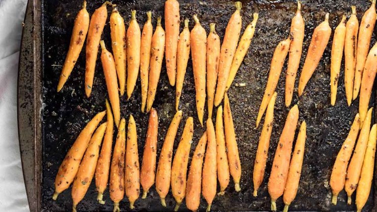 birds eye view of oven roasted maple glazed carrots on a baking tray garnished with fresh herbs