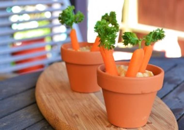 two vegan hummus carrot patches served in flower pots on top of a wooden surface