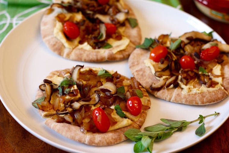 three vegan hummus pita pizzas on a white plate garnished with fresh herbs