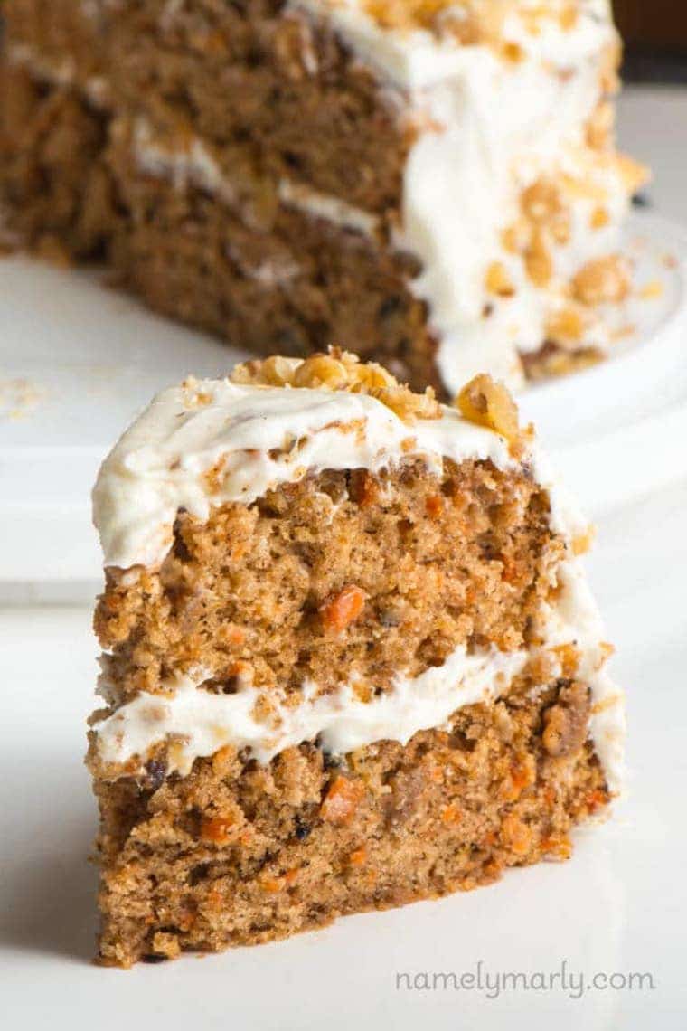 close up of double layered classic vegan carrot cake with additional carrot cake in the background garnished with walnuts