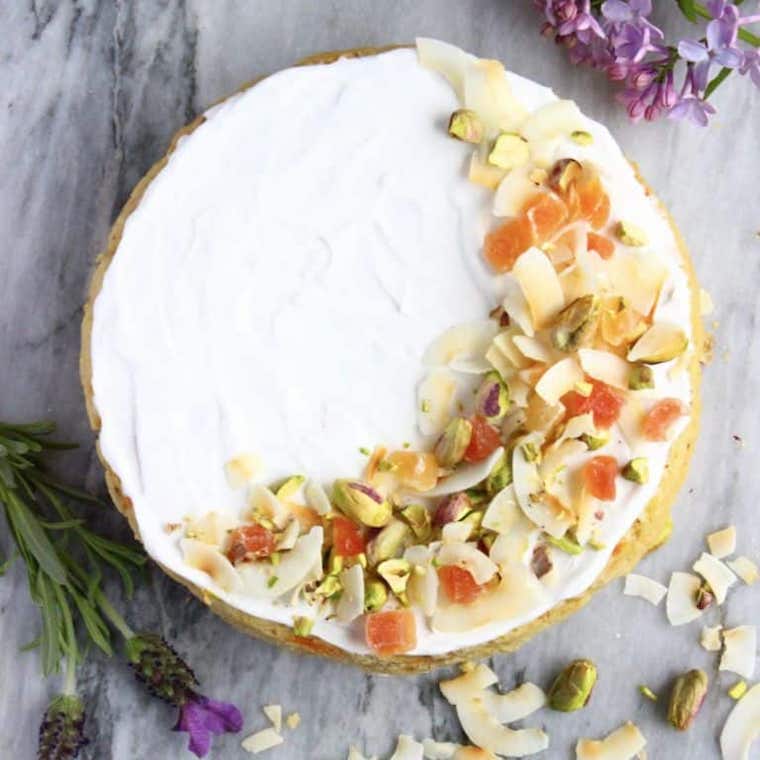 birds eye view image of gluten free tropical cake on a marble surface garnished with fresh fruit, coconut, and pistachios