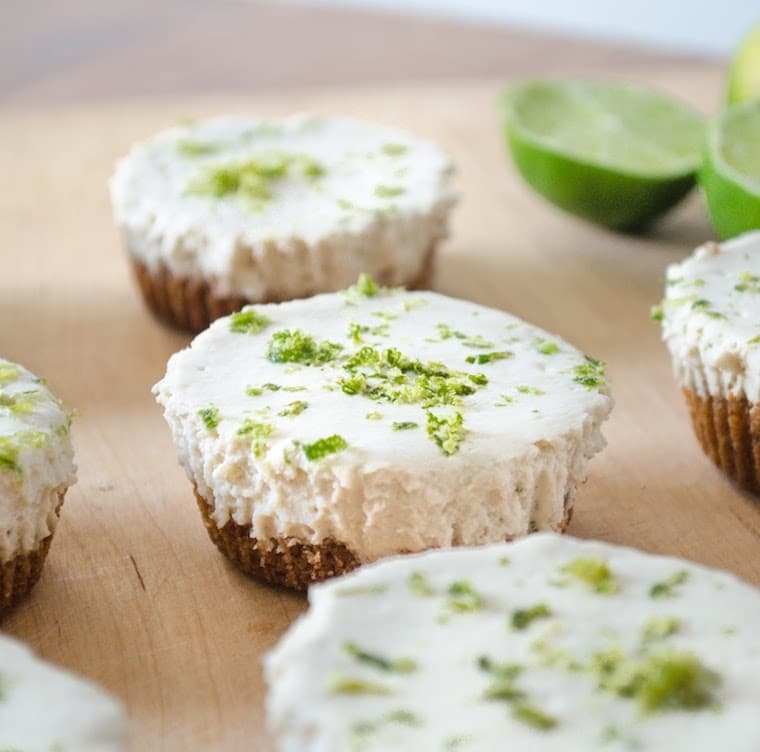 close up shot of vegan mini key lime pies garnished with lime zest on a wooden serving platter 