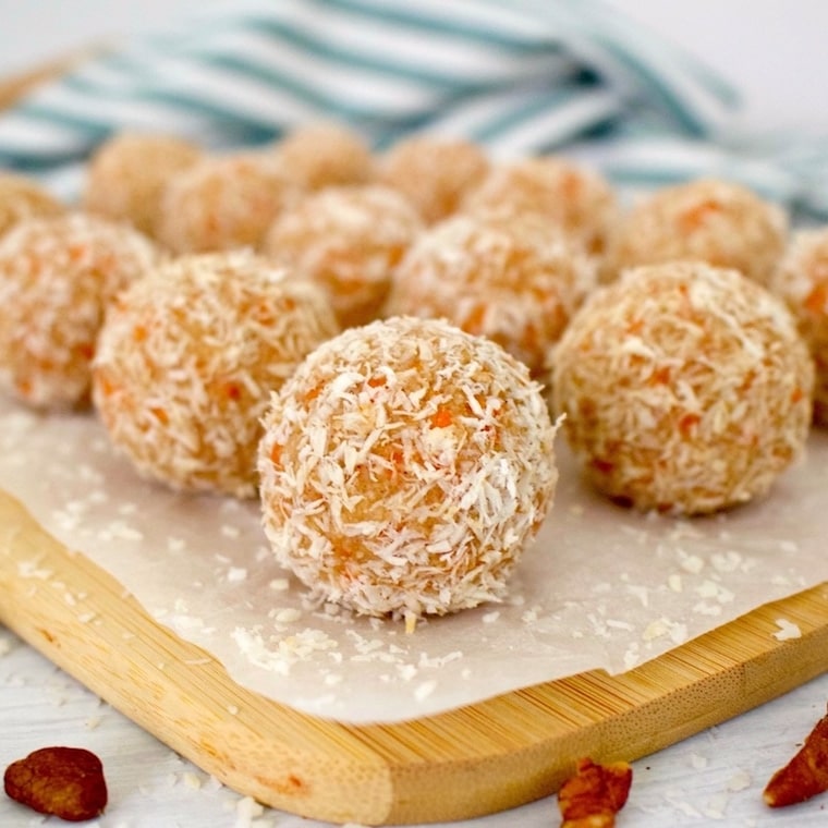 close up of gluten free vegan carrot cake bites rolled in coconut shreds served on a wooden platter