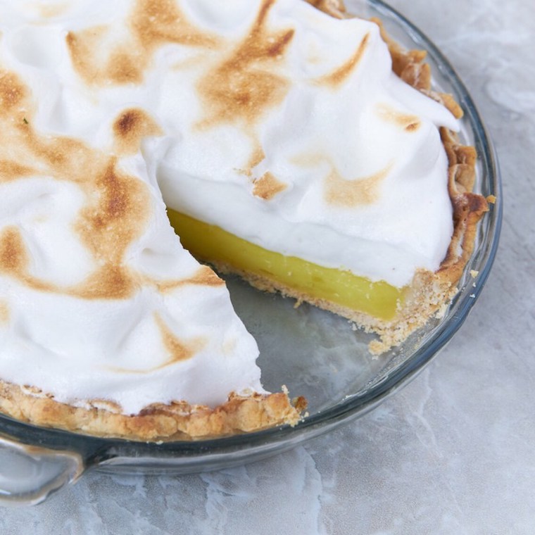 image of vegan lemon meringue pie in a glass dish on a marble counter