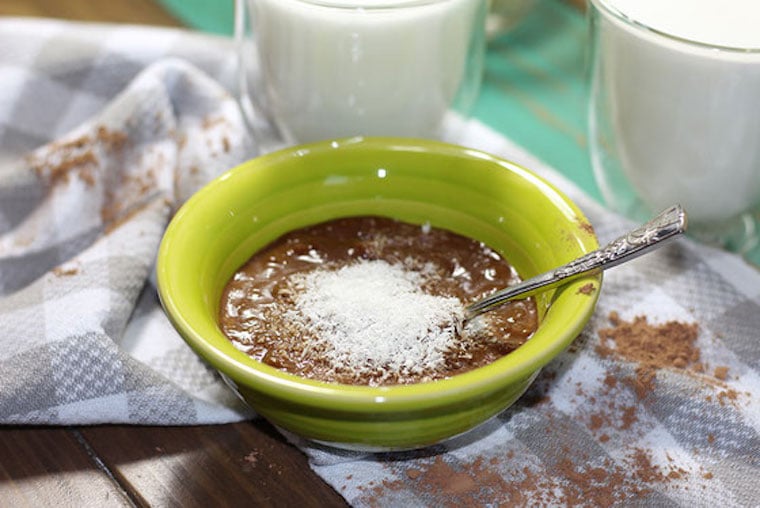 gluten free vegan healthy chocolate pudding in a green bowl with a silver spoon garnished with coconut shreds