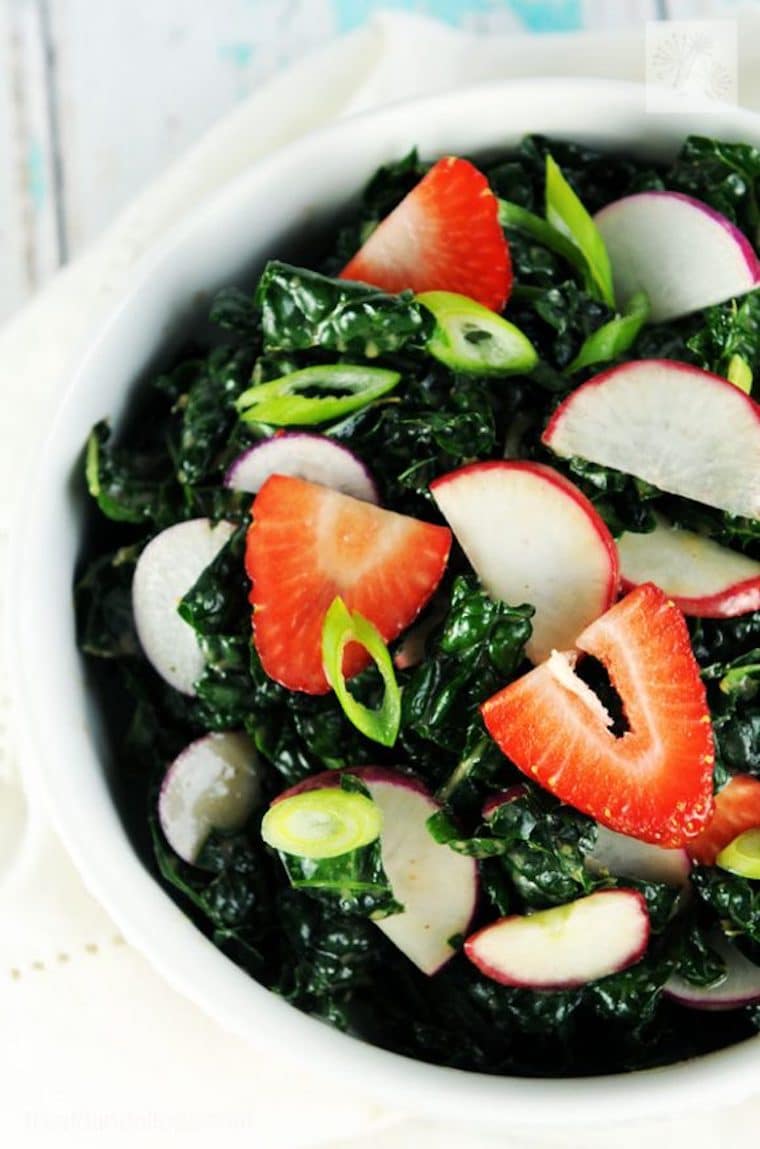 close up shot of vegan kale salad with strawberry vinaigrette garnished with green onions served in a white bowl