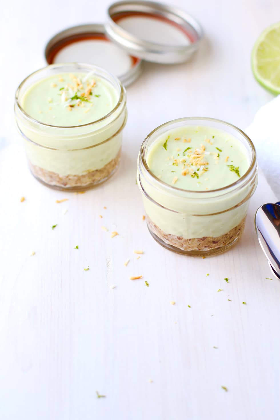 two vegan no bake coconut lime tartlets in small clear jars garnished with coconut and lime zest 