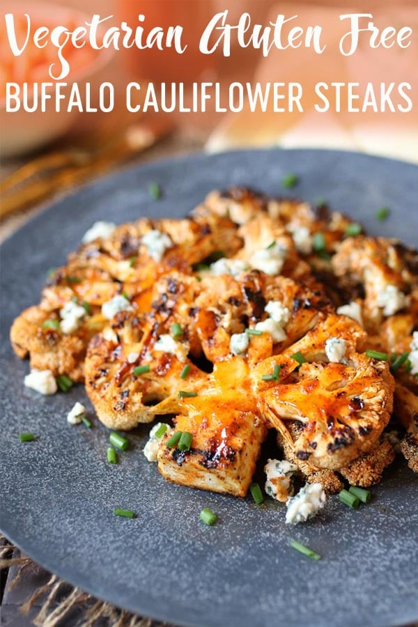 Buffalo cauliflower steaks on a grey plate topped with blue cheese and chives.