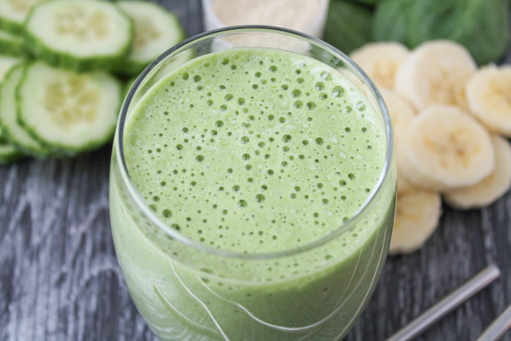 close up image of vegan green st. patrick's day shamrock shake in a clear glass with banana and cucumber slices in the background