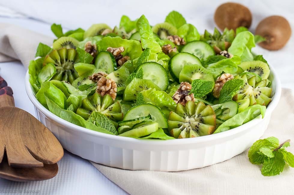 close up of kiwi cucumber salad with walnuts and fresh mint served in a large white dish with wooden serving utensils