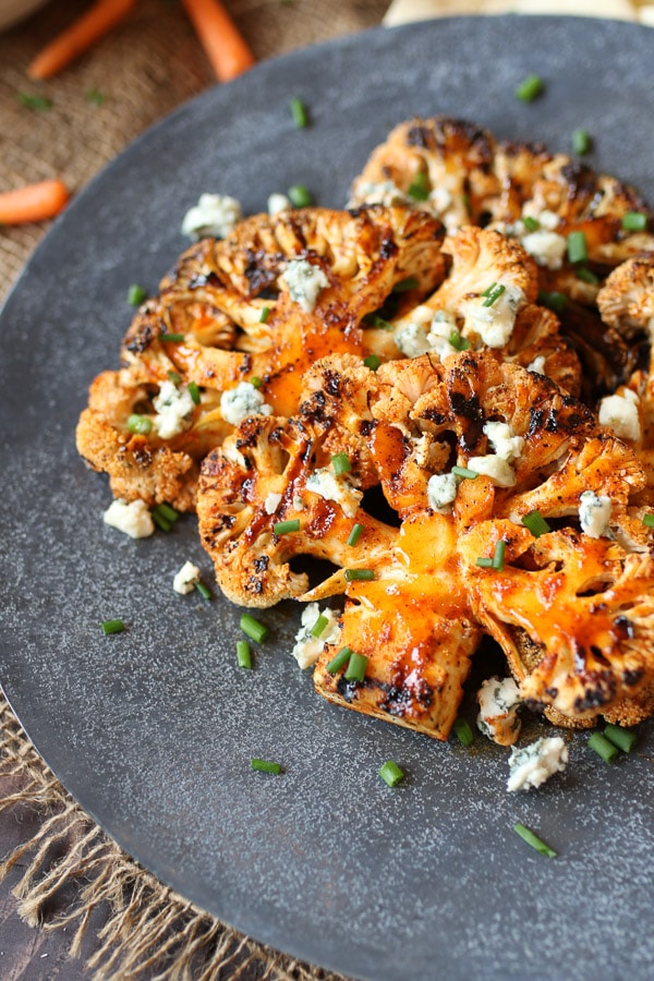 Buffalo cauliflower steak on a grey serving plate topped with blue cheese and chives.