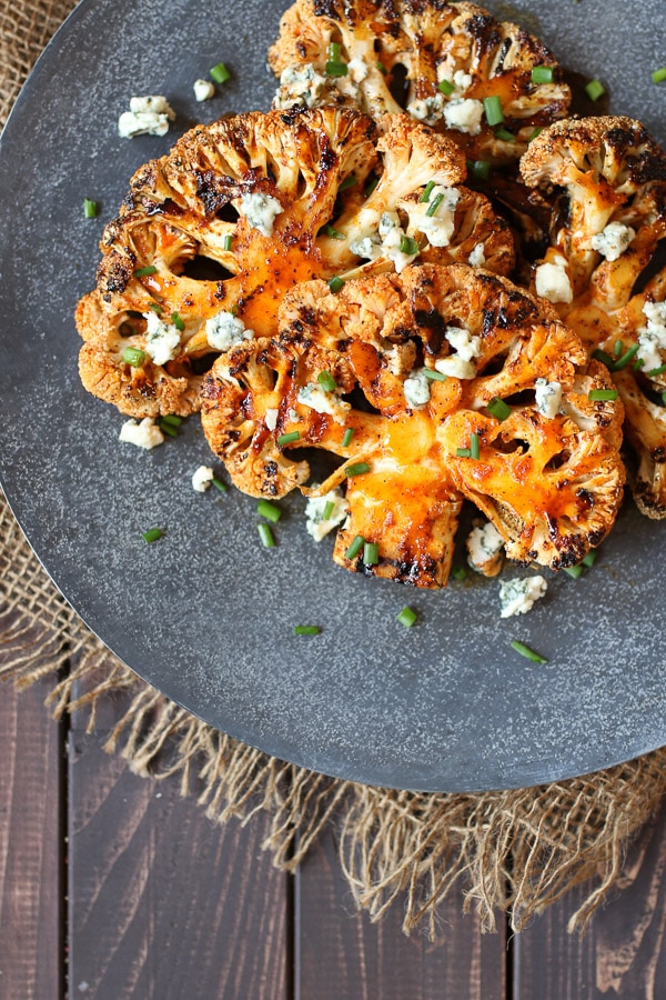 Buffalo cauliflower steaks topped with blue cheese and chives on a grey serving platter.