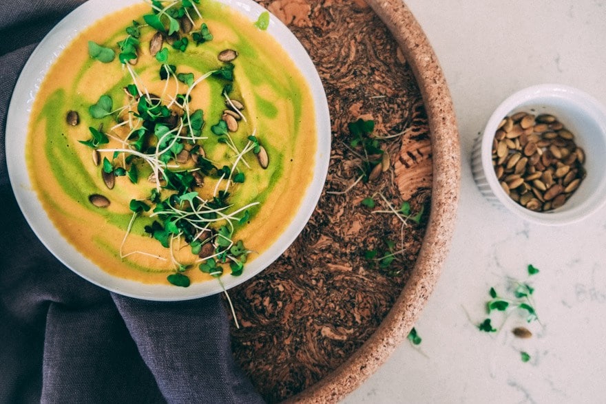 birds eye view of vegan and paleo green butternut squash soup garnished with fresh greens and pumpkin seeds on top of a wooden surface