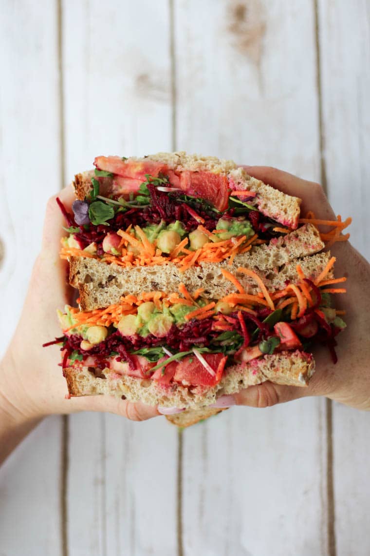 Birds eye view of two hands holding vegan sandwich with chickpea and avocado.