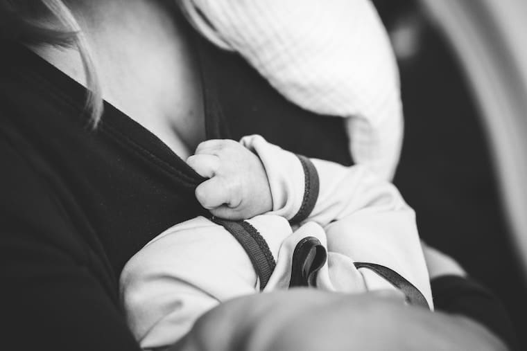 A newborn\'s hand holding the collar of a top while being held.