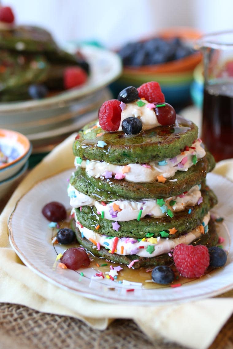 A stack of rainbow matcha protein pancakes topped with berries and maple syrup.