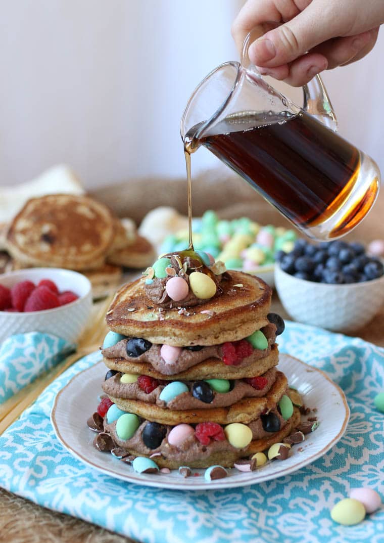 A stack of mini egg pancakes with maple syrup being poured over top for Easter morning breakfast.