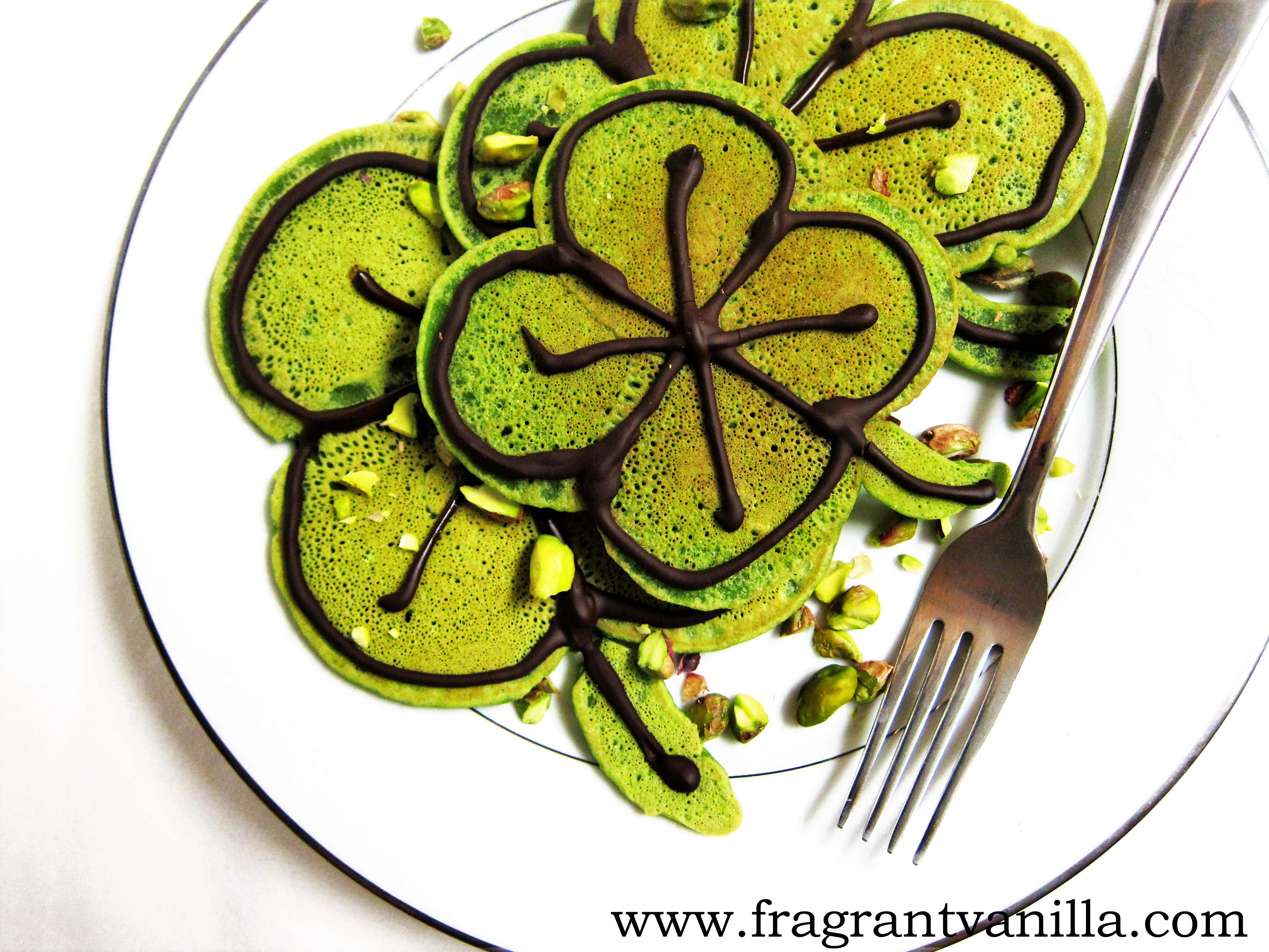 birds eye view of vegan st. patrick's day green shamrock pancakes served on a white plate with a silver fork garnished with chopped pistachios