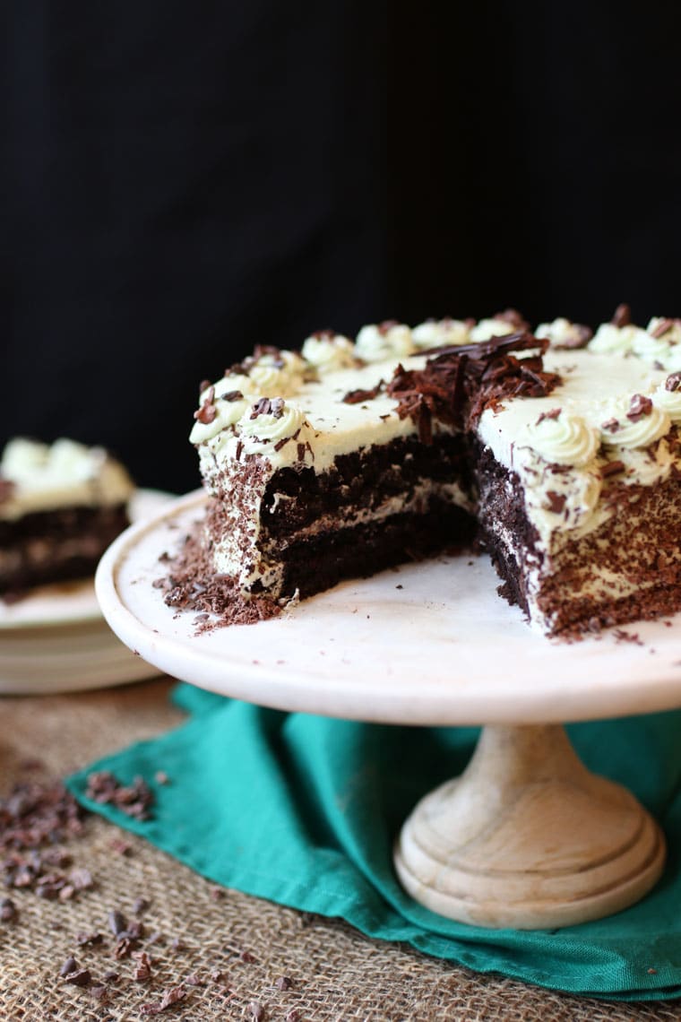 A chocolate mint cake on a cake stand with a slice cut out.