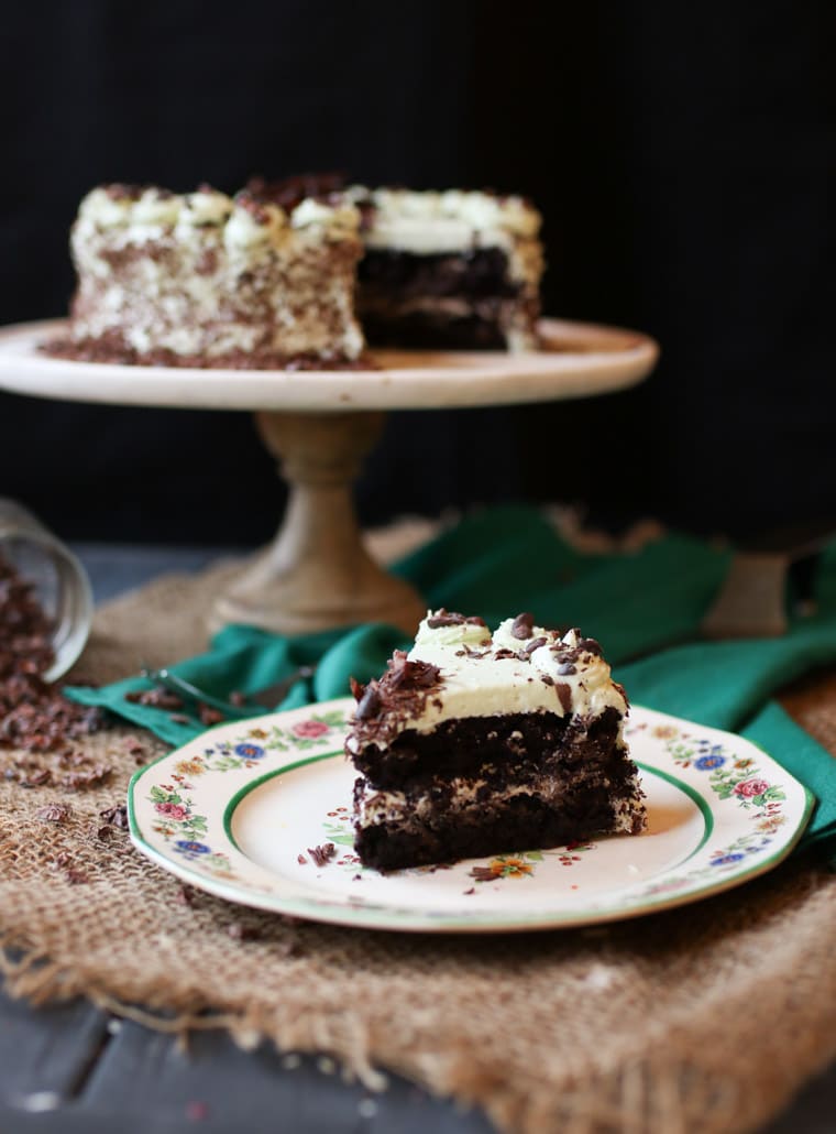 An image of a slice of chocolate mint cake with the whole cake in the background.