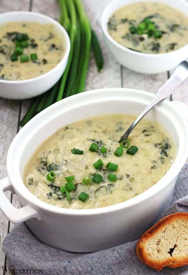 close up of a white ramekin containing vegan green colcannon soup garnished with green onions and a silver spoon inside