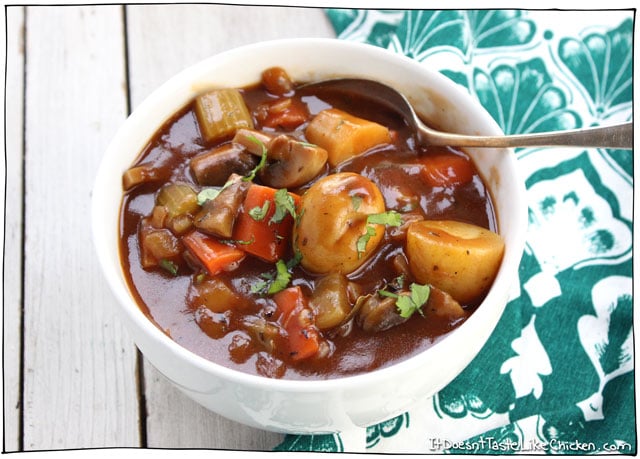 close up image of vegan vegan irish stew garnished with fresh herbs in a white bowl with a silver spoon