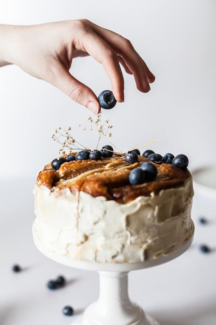Hand topping a cake with a blueberry. 