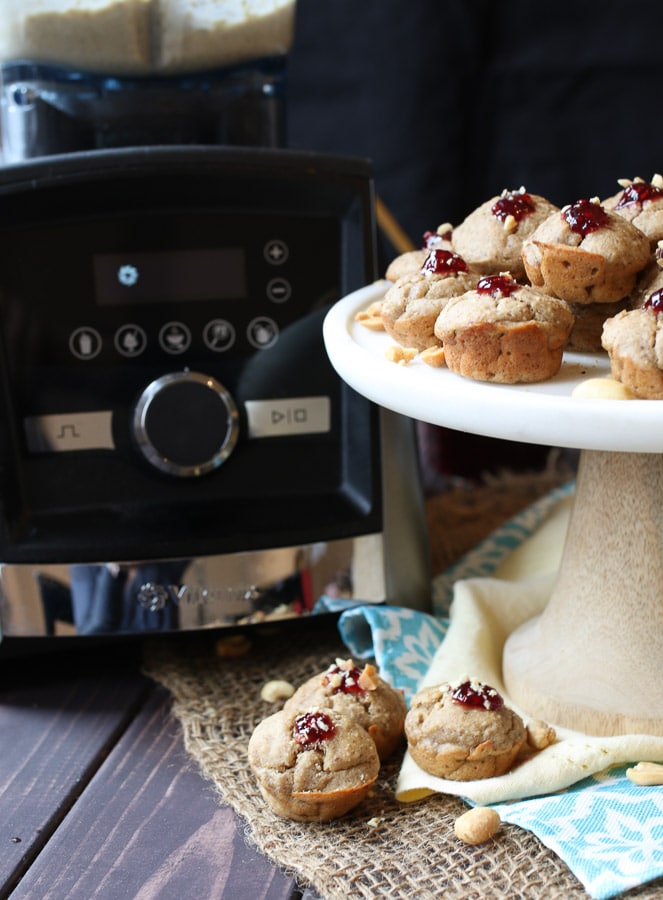 A white plate with blender muffins with jam on top and peanuts with a vitamix in the background.