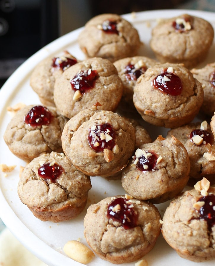 A close up of a mound of mini peanut butter and jelly muffins on a white plate. 