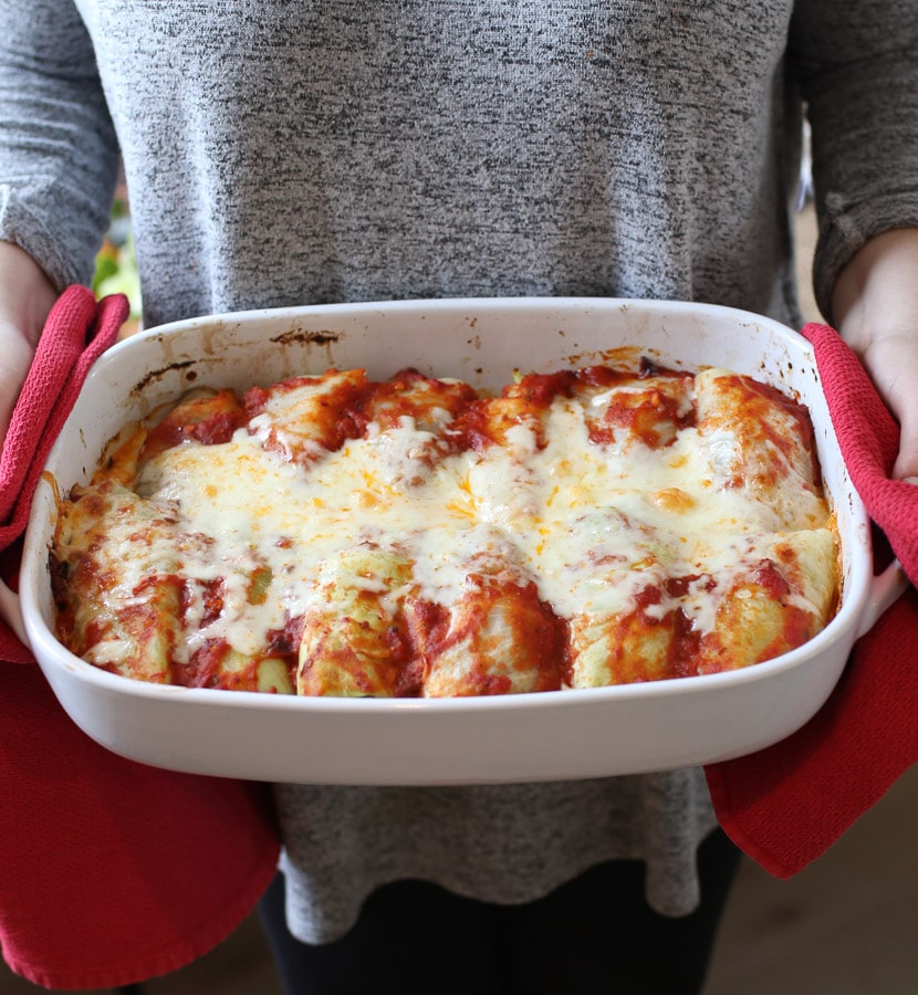 Person holding casserole dish with keto enchiladas.