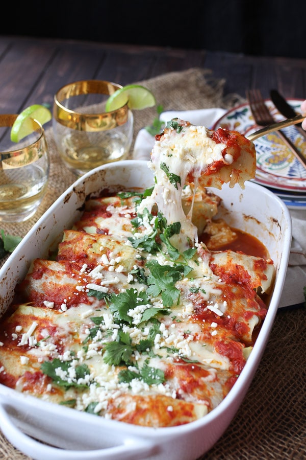 Spoon holding a serving of cheesy cabbage roll enchiladas in a white casserole dish. 