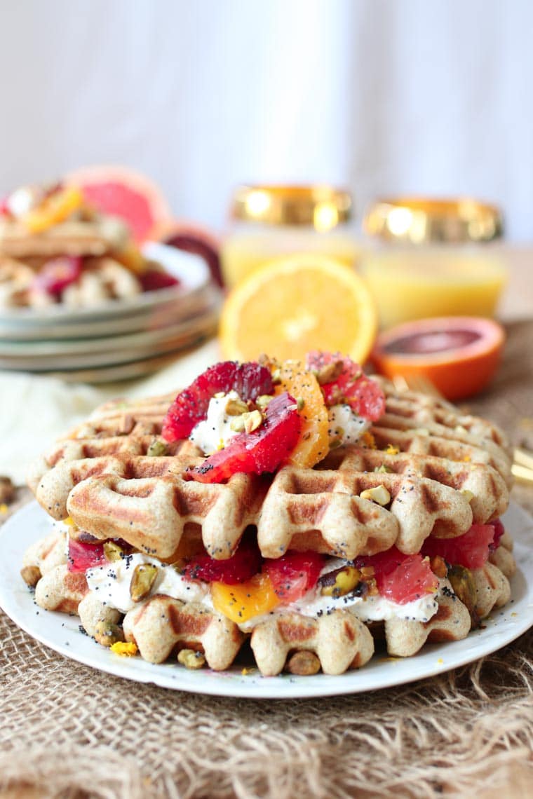 Stack of vegan orange poppyseed waffles topped with oranges. 