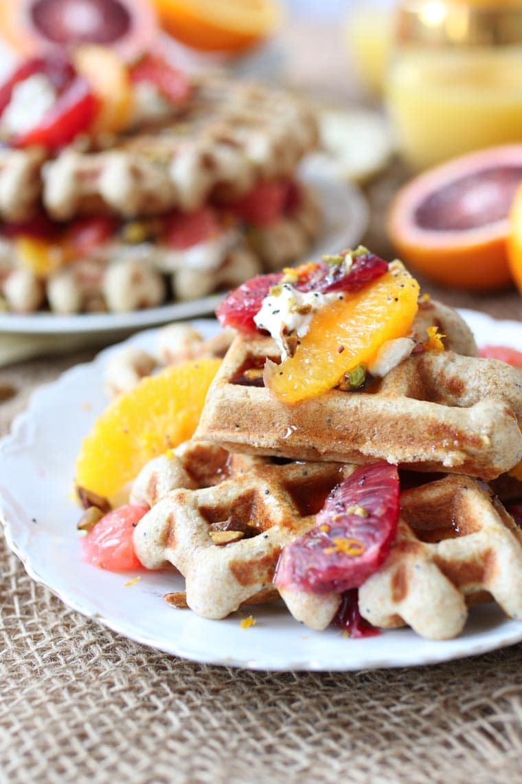 Close up of a plate of vegan orange poppyseed waffles topped with citrus segments. 