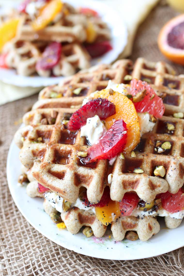 Close up of a plate of vegan orange poppyseed waffles topped with citrus segments and a dollop of yogurt. 
