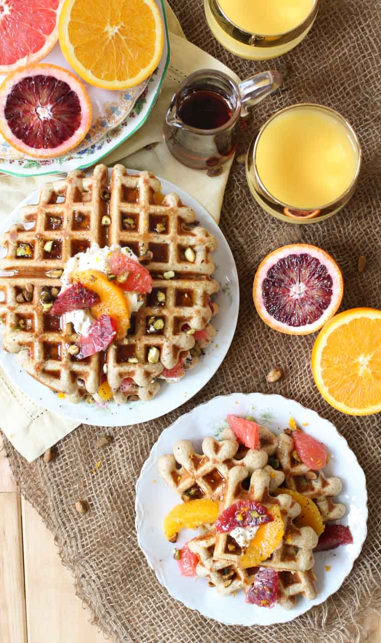 Overhead shot of a plate of vegan orange poppyseed waffles for brunch next to glasses of orange juice and maple syrup. 